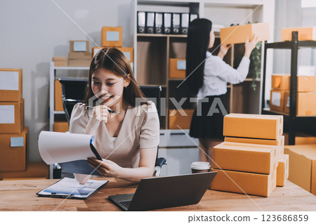 Startup SME small business entrepreneur of freelance Asian woman using a laptop with box Cheerful success Asian woman her hand lifts up online marketing packaging box and delivery SME idea concept 123686859