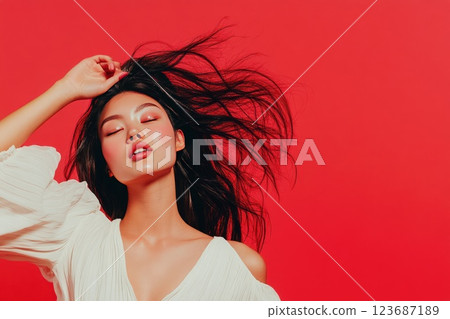 Confident woman with flowing hair poses against vibrant red background in expressive fashion statement 123687189