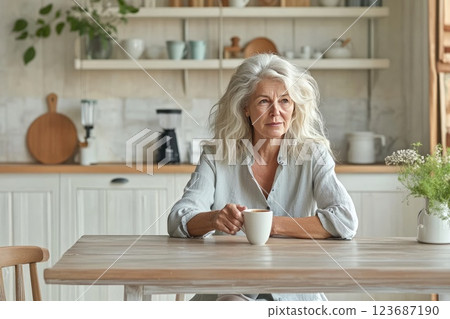 Mature woman enjoys a warm beverage while sitting at a kitchen table in a cozy setting Mature woman enjoys a warm beverage while sitting at a kitchen table in a cozy setting 123687190