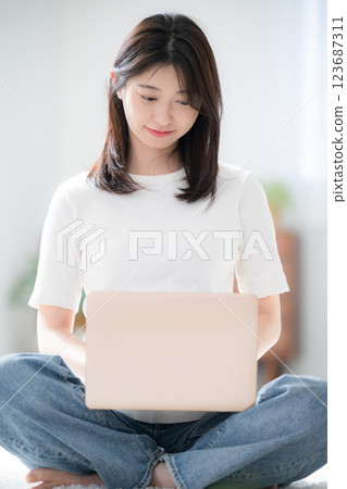 A young woman in casual clothes sitting cross-legged and looking down while using a computer in the living room 123687311