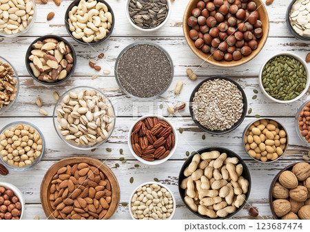 Mixed assorted raw healthy nuts and seeds in various bowls on light wooden table. 123687474