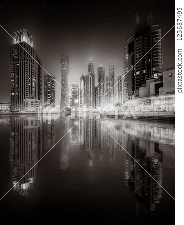 Urban city skyline with illuminated skyscrapers and waterfront railing in black and white at night, Dubai Marina bay UAE 123687495