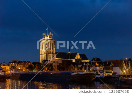 Dordrecht, South Holland, Holland - 09.07.2024: A beautifully illuminated historic church tower stands against a deep blue evening sky surrounded by charming houses and boats reflecting on calm waters Dordrecht, South Holland, Holland - 09.07.2024: A beautifully illuminated historic church tower stands against a deep blue evening sky surrounded by charming houses and boats reflecting on calm waters 123687668