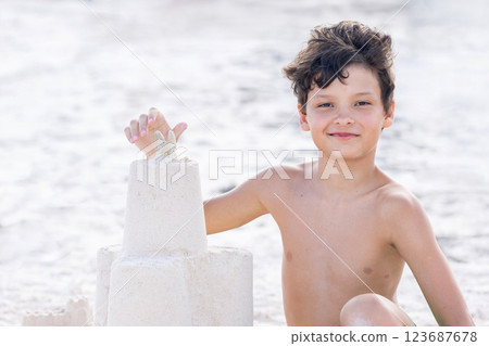 Teen boy is constructing a sand castle at the seashore beach. 123687678