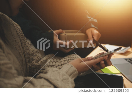 Startup small business SME, Entrepreneur owner African woman using smartphone or tablet taking receive and checking online purchase shopping order to preparing pack product box. 123689303