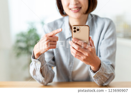 一位中年婦女在家裡的客廳微笑著指著她的智慧型手機 一位中年婦女在家裡的客廳微笑著指著她的智慧型手機 123690907