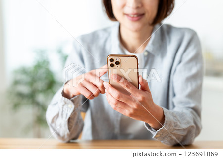 A middle-aged woman smiling while looking at her smartphone in the living room at home 123691069