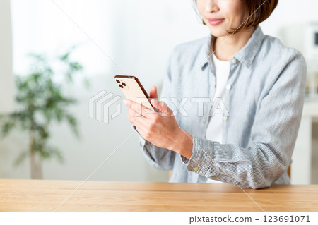A middle-aged woman smiling while looking at her smartphone in the living room at home 123691071