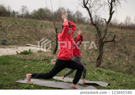 Siblings share joyful and engaging moments practicing yoga together in a tranquil natural environment under a beautifully cloudy sky Siblings share joyful and engaging moments practicing yoga together in a tranquil natural environment under a beautifully cloudy sky 123692580