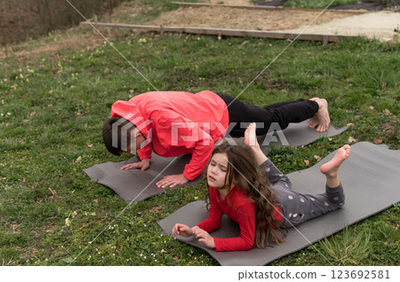Outdoor yoga practice with a parent and child on mats in a serene green environment during a cloudy day, showcasing bonding and wellness through exercise Outdoor yoga practice with a parent and child on mats in a serene green environment during a cloudy day, showcasing bonding and wellness through exercise 123692581