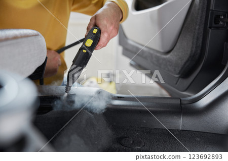 Service worker using cleaning properties of steam for cleansing car interior Service worker using cleaning properties of steam for cleansing car interior 123692893