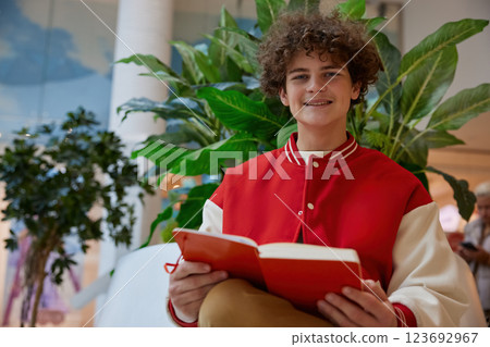 Happy teenage boy reading book while rest in shopping mall 123692967