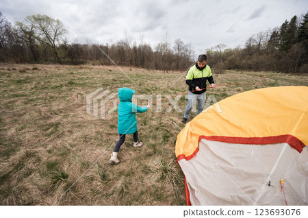 Creating family memories while camping in the great outdoors with a child pitching a tent on a cloudy afternoon in a serene nature setting Creating family memories while camping in the great outdoors with a child pitching a tent on a cloudy afternoon in a serene nature setting 123693076