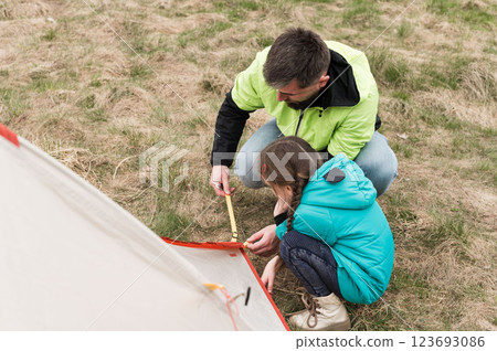 Family bonding under the open sky while setting up a colorful tent during a sunny day in the gentle spring grass, creating memories that last forever 123693086