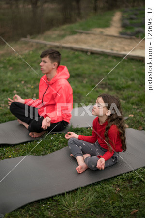 Mindful moments in nature as a boy and girl practice yoga on mats, embracing tranquility during a serene afternoon under the soft glow of sunlight 123693112