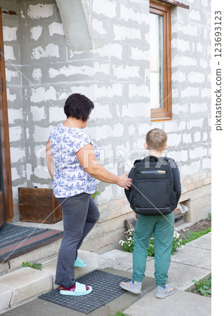 A woman sees her grandson off to school, gently placing a hand on his back as he prepares to leave, showing love and support. 123693123