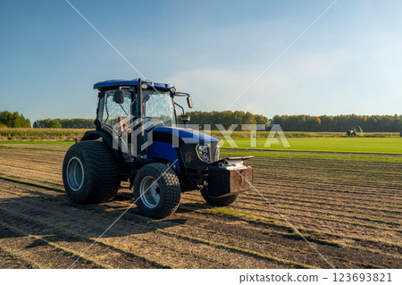 A Blue Tractor is Actively Working on a Lush Green Field at the Beautiful Sunrise Hour A Blue Tractor is Actively Working on a Lush Green Field at the Beautiful Sunrise Hour 123693821