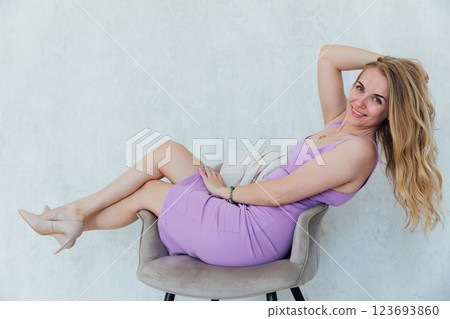 Beautiful blonde woman sitting on a chair in purple summer dress 123693860