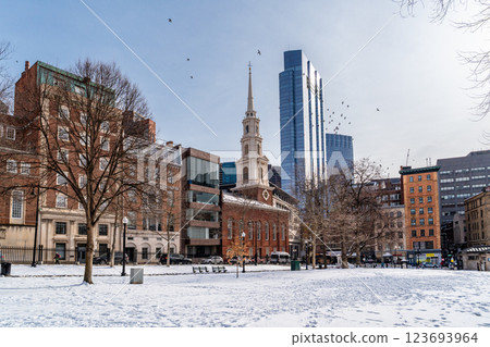 View of Park Street Church and surrounded buildings in Boston during winter with snow on the Boston Common ground and flock of birds flying against clear blue sky 123693964