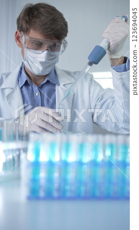Male scientist researcher, wearing lab coat, white medical gloves, mask and protective glasses is using micropipette filling test tubes in modern laboratory. Low key lighting. Science concept 123694045