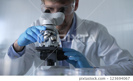 Male scientist researcher wearing blue gloves, protective glasses is using microscope in modern laboratory, portrait view. Low key lighting photo. Science and Medicine concepts 123694067