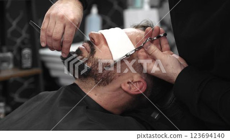 Professional barber carefully trimming beard with scissors, creating clean lines and sharp detailing inside contemporary barbershop workspace Professional barber carefully trimming beard with scissors, creating clean lines and sharp detailing inside contemporary barbershop workspace 123694140