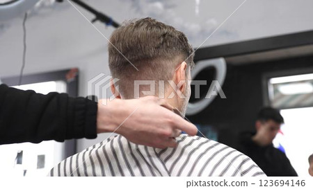 Skilled barber trimming client's neck hairline, wielding straight razor with expertise in traditional, vintage style barbershop setting 123694146