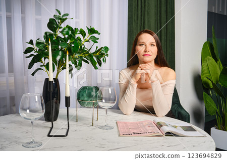 Middle-aged woman seated at a stylish table with greenery and glassware in a modern interior 123694829