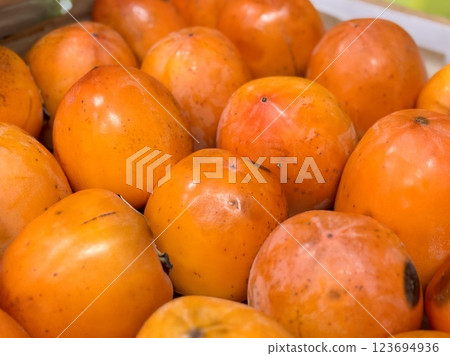A pile of ripe juicy orange persimmons in a box, on sale at a supermarket vegetable stand, showcases organic, vegetarian and healthy food. Close-up 123694936