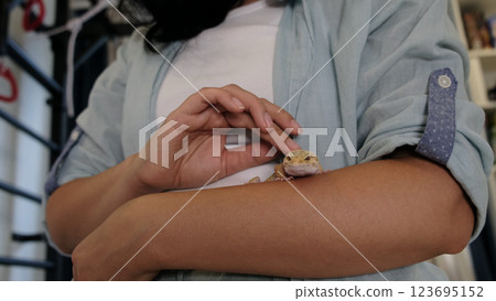 The gecko calmly rests on the arm of its owner, showcasing the growing bond between human and exotic pet. This image symbolizes care, patience, and the peaceful coexistence of nature and humans. The gecko calmly rests on the arm of its owner, showcasing the growing bond between human and exotic pet. This image symbolizes care, patience, and the peaceful coexistence of nature and humans. 123695152