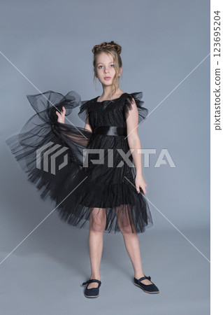 A young girl in a black tulle dress twirls gracefully, holding the fabric to show off its flowy layers. This image highlights elegance and sophistication in children's fashion, showcasing a formal and A young girl in a black tulle dress twirls gracefully, holding the fabric to show off its flowy layers. This image highlights elegance and sophistication in children's fashion, showcasing a formal and 123695204