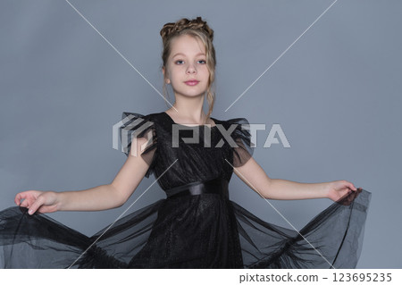 A girl gently lifts the sides of her black dress, showing off the dress's sheer layers and ruffled design. The scene emphasizes grace and confidence, showcasing the intersection of fashion and A girl gently lifts the sides of her black dress, showing off the dress's sheer layers and ruffled design. The scene emphasizes grace and confidence, showcasing the intersection of fashion and 123695235