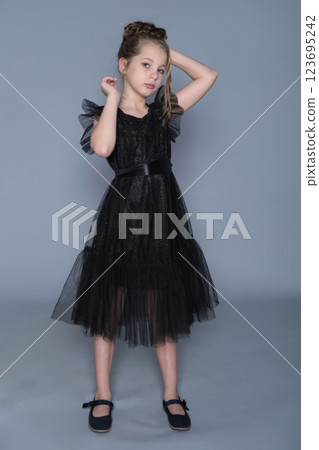 A girl in a black dress with tulle ruffles poses gracefully, showcasing the dress's intricate layers. The scene highlights sophistication in children's clothing, promoting timeless style and youthful A girl in a black dress with tulle ruffles poses gracefully, showcasing the dress's intricate layers. The scene highlights sophistication in children's clothing, promoting timeless style and youthful 123695242