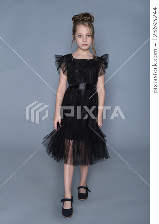 A young model in a black dress strikes a delicate pose, drawing attention to the layered skirt and detailed design. This image reflects the beauty of children's fashion, with an emphasis on refined A young model in a black dress strikes a delicate pose, drawing attention to the layered skirt and detailed design. This image reflects the beauty of children's fashion, with an emphasis on refined 123695244