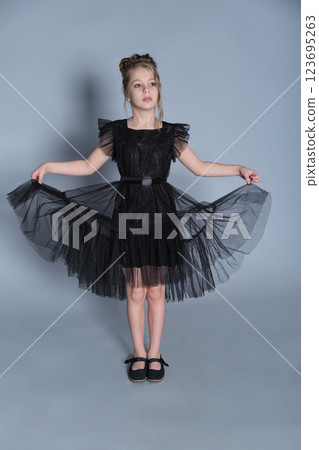 A girl poses confidently in a black ruffled dress, lifting the skirt to reveal the delicate layers of tulle. The photo captures both elegance and playfulness, emphasizing modern trends in children's 123695263
