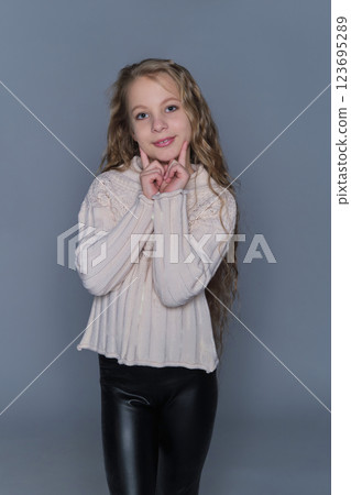 A young girl with long, wavy hair gently rests her hands on her cheeks, wearing a cozy knit sweater. This image emphasizes natural beauty and children's winter fashion, showcasing warmth and comfort. 123695289