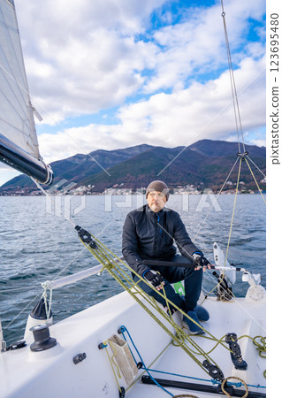 Man sailing a sports yacht in the Kotor Bay, Montenegro, showcasing adventure, freedom, and nautical sport. Man sailing a sports yacht in the Kotor Bay, Montenegro, showcasing adventure, freedom, and nautical sport. 123695480