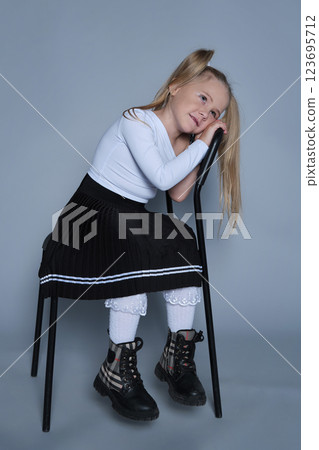 fun moment from a children's fashion shoot, where a 5-year-old girl, dressed in a trendy outfit, sits playfully on a chair. Her bright laughter and energetic pose make this image perfect for kids 123695712
