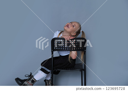 A playful 5-year-old girl is photographed in a studio, sitting on a black chair with a big, joyful expression. Dressed in a stylish one-shoulder top and black pleated skirt, she radiates energy and A playful 5-year-old girl is photographed in a studio, sitting on a black chair with a big, joyful expression. Dressed in a stylish one-shoulder top and black pleated skirt, she radiates energy and 123695728