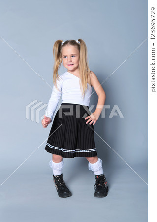 young girl showcases a chic look in a one-shoulder white top paired with a black pleated skirt and black boots. Her confident stance and playful expression bring out the modern trends in children's young girl showcases a chic look in a one-shoulder white top paired with a black pleated skirt and black boots. Her confident stance and playful expression bring out the modern trends in children's 123695729