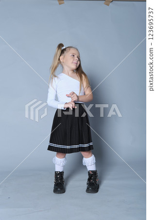 playful and confident little girl poses with her hand on her hip and a smile on her face. Dressed in a trendy one-shoulder top and black skirt, her personality shines through in this lively portrait playful and confident little girl poses with her hand on her hip and a smile on her face. Dressed in a trendy one-shoulder top and black skirt, her personality shines through in this lively portrait 123695737