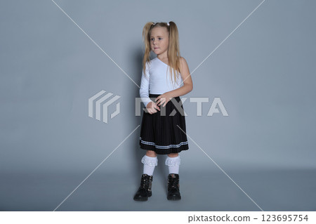 young girl strikes a powerful pose, her hand on her hip and her gaze forward. Dressed in a stylish one-shoulder top and pleated skirt, her outfit and stance exude confidence, making this image great young girl strikes a powerful pose, her hand on her hip and her gaze forward. Dressed in a stylish one-shoulder top and pleated skirt, her outfit and stance exude confidence, making this image great 123695754