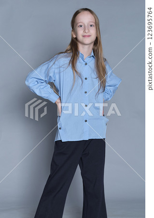 Smiling girl with hands on hips in a blue shirt, exudes confidence. Perfect for themes of youth empowerment and fashion. Smiling girl with hands on hips in a blue shirt, exudes confidence. Perfect for themes of youth empowerment and fashion. 123695764