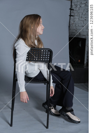 Pensive girl leaning on chair, her attire speaking of cozy days. Suitable for educational or lifestyle-focused narratives. Pensive girl leaning on chair, her attire speaking of cozy days. Suitable for educational or lifestyle-focused narratives. 123696185