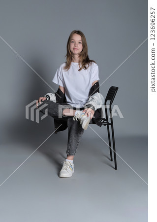 A teenage girl sits casually in a chair, her gaze steady and assured. Her posture reflects the self-confidence and ease of todays youth, embracing a minimalist style. A teenage girl sits casually in a chair, her gaze steady and assured. Her posture reflects the self-confidence and ease of todays youth, embracing a minimalist style. 123696257