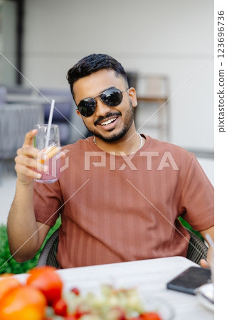 Handsome man sitting outside at a restaurant table and drinking iced beverage in cafe 123696736