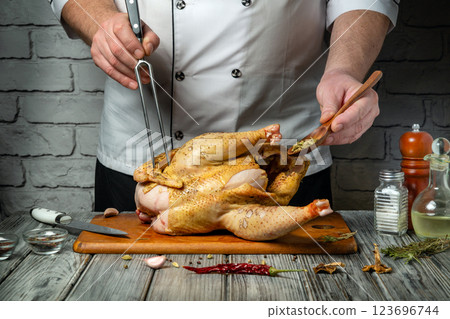 Inside a rustic kitchen, a skilled chef meticulously seasons and carves a perfectly roasted chicken. Fresh herbs and spices enhance the dish, creating an inviting atmosphere for cooking enthusiasts 123696744