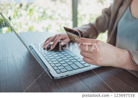 Woman holding credit card while using laptop and shopping outdoor at coffee shop, 123697538