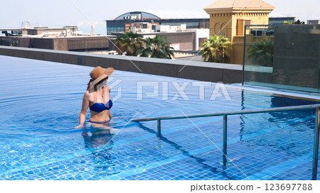 Woman in bikini and hat exits swimming pool holding onto handrail Woman in bikini and hat exits swimming pool holding onto handrail 123697788