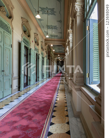 Perspective hallway leading with ceiling hanging lamp, green doors, columns and window leading into entrance green ancient door. 123698049